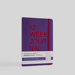 A purple notebook with '12 Week Journal' written on the cover in red text. It has rounded corners and an elastic closure.