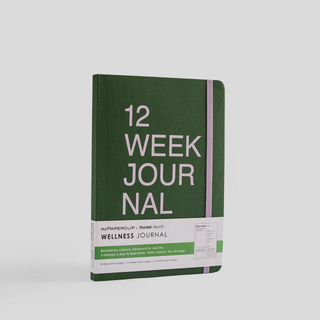 A dark green notebook with '12 Week Journal' written on the cover in pale purple text. It has rounded corners and an elastic closure.