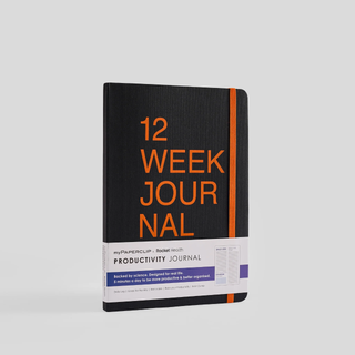 A black notebook with '12 Week Journal' written on the cover in orange text. It has rounded corners and an elastic closure.